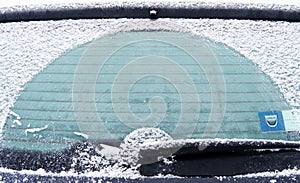 Close-up of snow-covered car rear with frozen windshield and wiper on winter morning