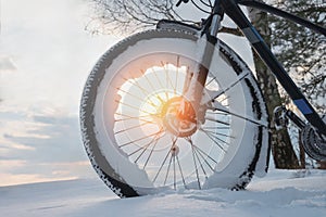 Close-up of a snow-covered wheel of a standing bicycle in the light of the setting sun in the countryside. Winter evening. Low