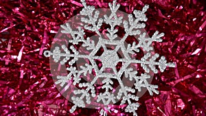 A close-up snowflake lies on New Year`s red tinsel and slowly moves clockwise. Christmas winter background. Happy New Year