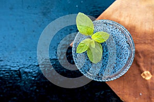 Close up of soaked sabja seeds or falooda seeds or sweet basil seeds in a glass bowl on brown colored napkin on wooden surface wit