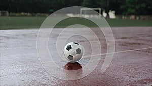 Close-up of soccer ball that lies on the stadium treadmill in heavy rain against the background of a football goal. The