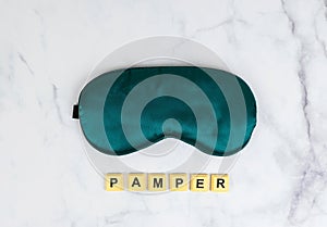 Close up of soft clean green satin sleeping mask on white background with the word pamper, self care concept