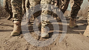 Close-up of soldiers boots marching in unison through sandy terrain