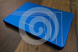 Close-up: A solid-state drive in a blue metal case lies on a surface with a wooden texture