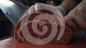 Close-up of somebody`s hands in protective gloves neatly chopping the meat on the cutting board. Action. Cutting meat