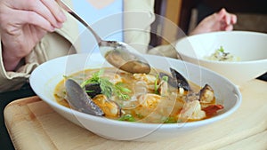 Close-up, someone eats tom yam with mussels with a spoon from a white plate