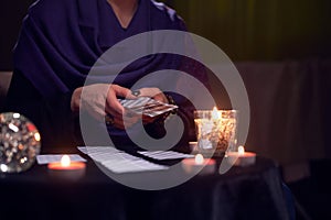 Close-up of soothsayer female guessing on cards sitting at table with burning candles, magic ball