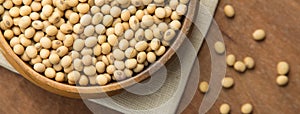 Close up of soybeans in wooden bowl putting on linen and wooden background. Banner with copyspace.