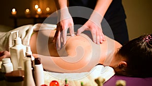 Close-up spa massage woman`s shoulders and back. Male hands do massage to a woman in a dark room with candles in the