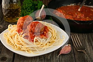 Close-up of spaghetti with meatballs and a pan with meatballs in tomato sauce with garlic and onions on a rustic table