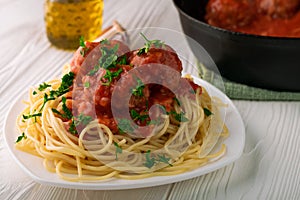 Close-up of spaghetti with meatballs with tomato sauce and parsley in white plate and black pan with meatballs