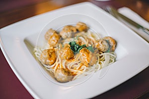 Close-up of spaghetti pasta with meatballs and tomato sauce in a white plate on the table