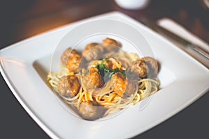 Close-up of spaghetti pasta with meatballs and tomato sauce in a white plate on the table