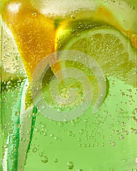 Close-up of sparkling fresh lemonade with ice, slices of lime, lemon and colored plastic straws in glass with large