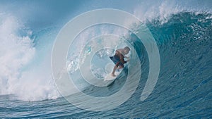 CLOSE UP: Spectacular shot of young surfboarder riding a big emerald tube wave.