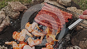 Close up speed video of man cooking some sausages and chicken wings outdoors in wild