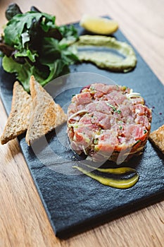 Close up Spicy Bluefin Tuna Tartare with sour and spicy sauce. Served with toast and salad on black stone plate