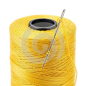 Close-up of a spool of bright yellow thread with a sewing needle threaded through it on a white background