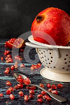 Close-up of spoon with pomegranate seeds, white colander with wet red pomegranate and seeds, with selective focus, on blue marble,
