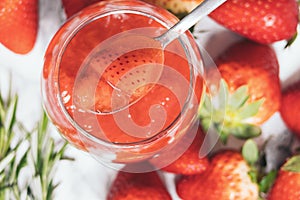 Close up of a spoon is scooping up a fresh strawberry jam from a glass jar