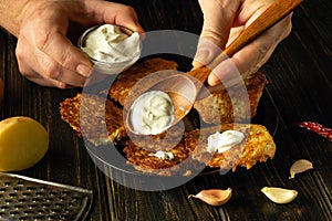 Close-up of a spoon with sour cream in the hand of a chef. Preparing a breakfast dish with potato pancakes and sour cream.