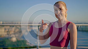 Close-up. sportive young girl runner approvingly shows thumbs up gesture. Girl with wireless headphones. 4K