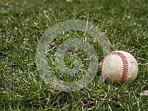 Close up sports background image of an old used weathered leather baseball ball laying in the grass field outside showing