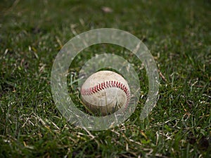 Close up sports background image of an old used weathered leather baseball ball laying in the grass field outside showing