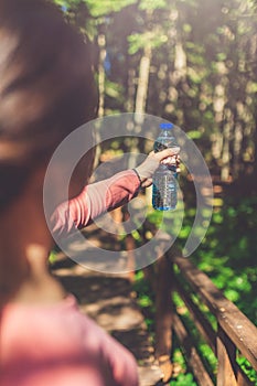 Close up of sportswoman holding bottle of water in forest. Nature and healthy lifestyle concept