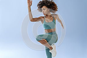 Close up of sporty woman running in Mid-Air exercising during cardio workout over studio background