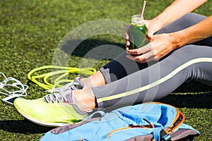 Close Up Sporty young woman holding green juice sitting on grass