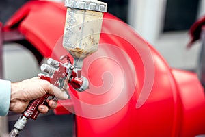 Close-up of spray gun with red paint painting a car