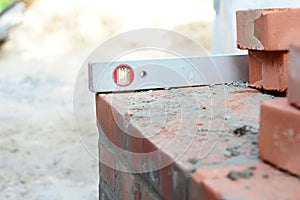 A close-up on a sprit level used to level the corner brick courses on a mortar bed while bricklaying the wall of the house