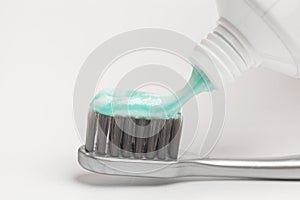 Close up of squeezing toothpaste on toothbrush on white background.