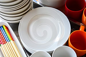 Close up stack of blank clean white dishes, bowls, plates, mugs and colorful wooden chopsticks on metal tray, copy space