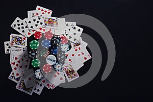 Close up stack of different colored poker chips, playing cards and dices isolated over black casino table background with copy
