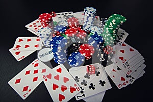Close up stack of different colored poker chips, playing cards and dices isolated over black casino table background. Gambling