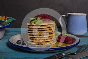 Close-up of a stack of Dutch waffles with raspberries, blueberries and honey on blue wooden background. Isolated image