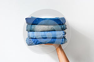 Close up stack of folded denim blue jeans in hand over white color wall background