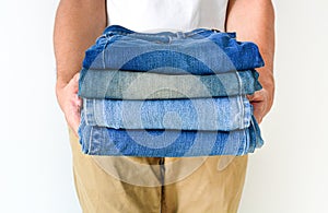 Close up stack of folded denim blue jeans in hand over white color wall background