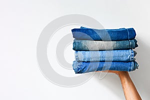 Close up stack of folded denim blue jeans in hand over white color wall background, copy space