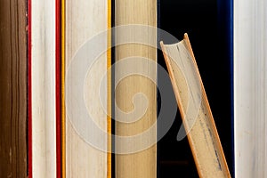 Close up stack of old books vertically placed on the wooden shelf