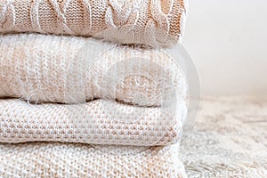 Close up of stacked wool knitted sweaters or jumpers, in white and light tones, cozy image, soft fabrics in white background