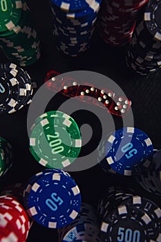 Close up stacks of different colored poker chips and playing dices on the casino table isolated over black background. Gambling