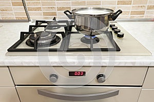 Close-up of stainless steel cooking pot on gas stove in contemporary upscale modern home kitchen. Selective focus on pot.