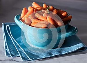 A close up of steamed baby carrots in a blue bowl ready for serving.