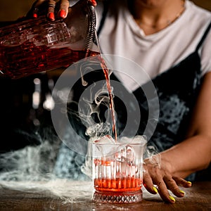 close-up of steaming glass with ice cubes into which the bartender pours cocktail