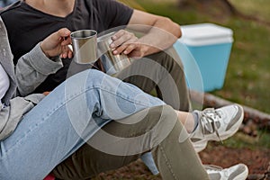 Close up of steel cups with coffee or tea in hands of couple. Picnic concept. Happy together.