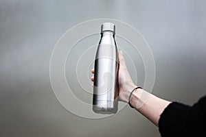 Close-up of steel thermo bottle in hand of young girl.