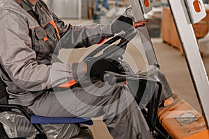 Close - up steering wheel and levers. man driving a forklift through a warehouse in a factory. driver in uniform and
